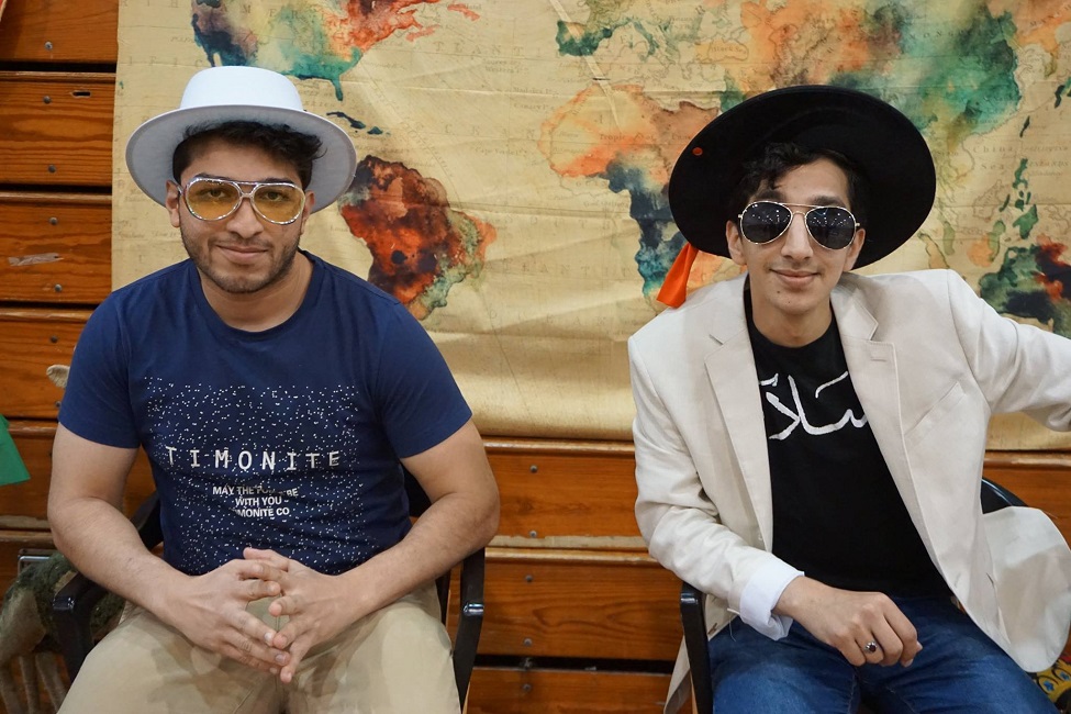 Two students wearing sunglasses sitting in front of the world map