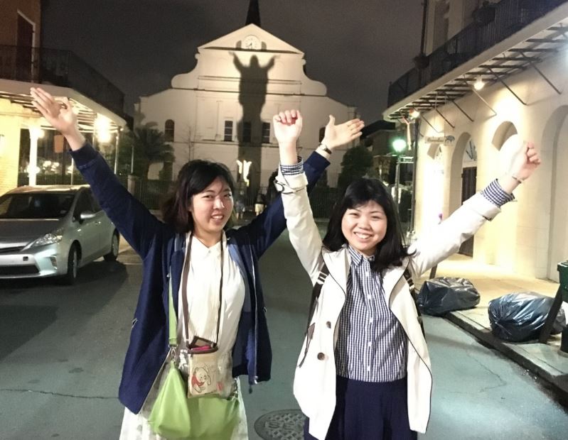 two girls posing with arms in the air, in front of the shadow cast by the statue of Jesus