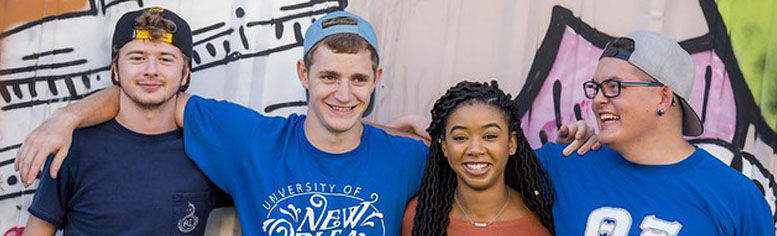 4 UNO Students, arms around each other, smiling for a group photo