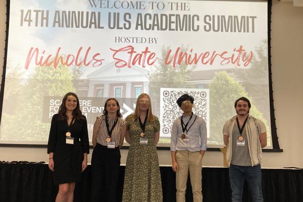 Five UNO students stand on stage at the 14th Annual ULS Academic Summit
