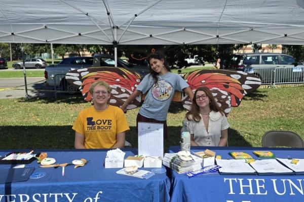Three students standing behind the University of New Orleans tables at Bug Fest