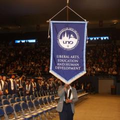 A student ambassador carries the banner for the College of Liberal Arts, Education, and Human Development